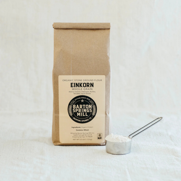 Kraft bag of Barton Springs Mill Organic Einkorn Whole Grain Flour with a metal scoop of flour beside it.