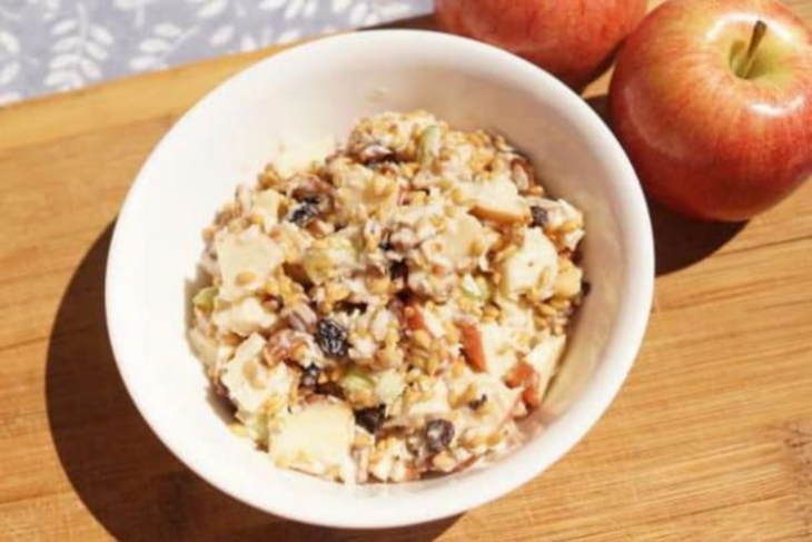 Einkorn apple salad with wheat berries, celery and raisins in a bowl beside fresh apples