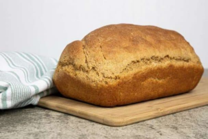 Einkorn whole grain bread loaf on a wooden board with a striped towel.